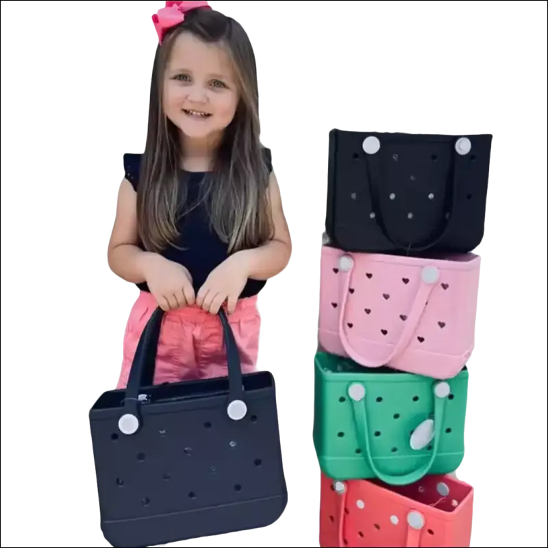 Young girl holding a colorful perforated handbag with several similar bags stacked beside her.